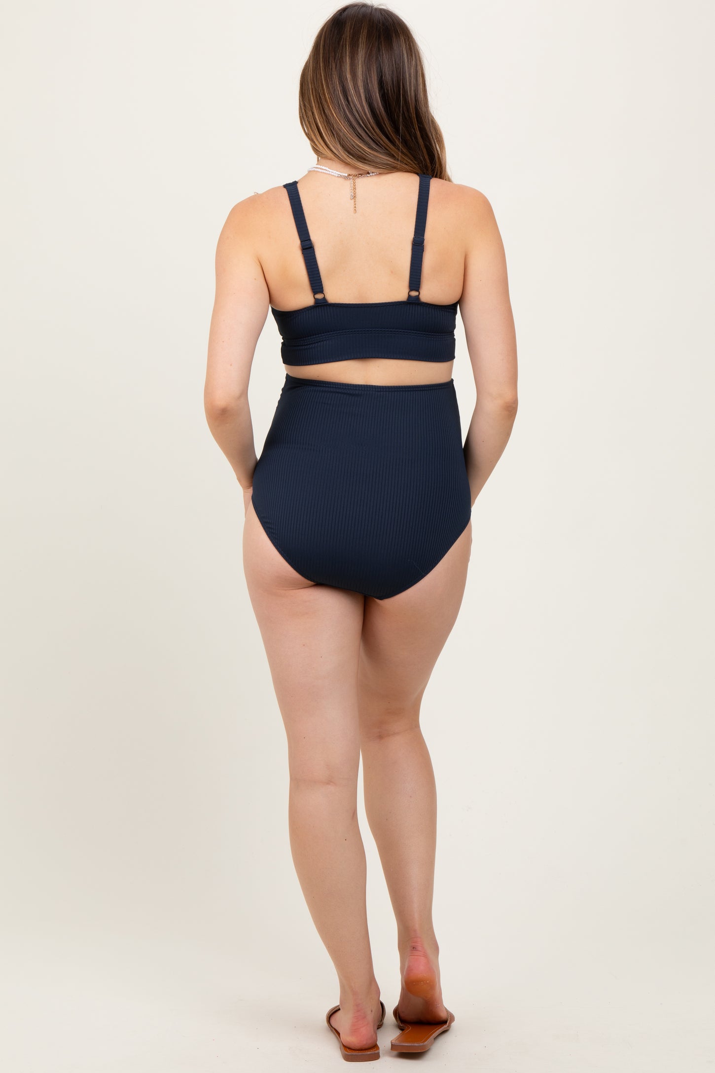woman wearing a navy blue ribbed maternity bikini set with a high-waisted bottom and adjustable straps