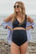 woman wearing a black maternity bikini top and high-waisted bottoms, smiling on the beach with a blue shirt over her shoulders