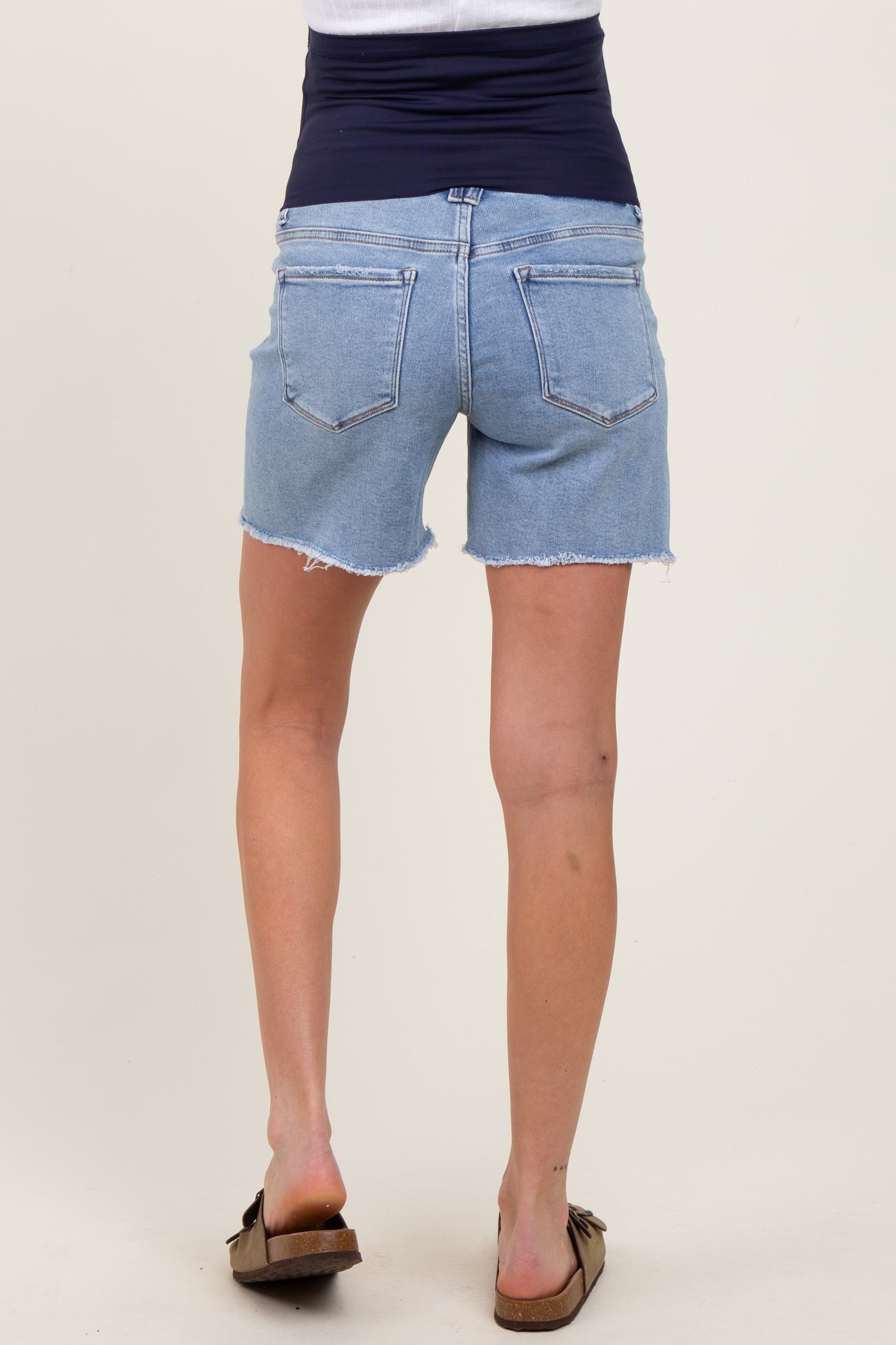 woman wearing a pair of light blue maternity denim shorts with a frayed hem and a stretchy navy waistband