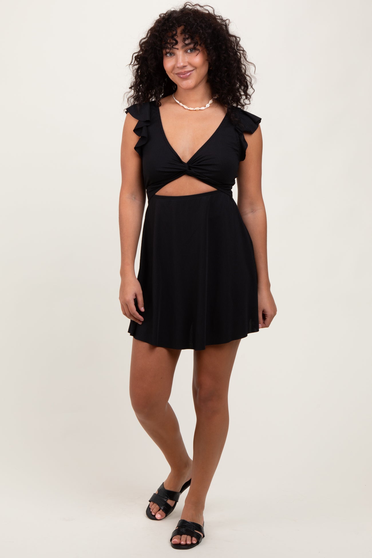 woman wearing a black short dress with ruffle sleeves and a cut-out design, paired with black sandals