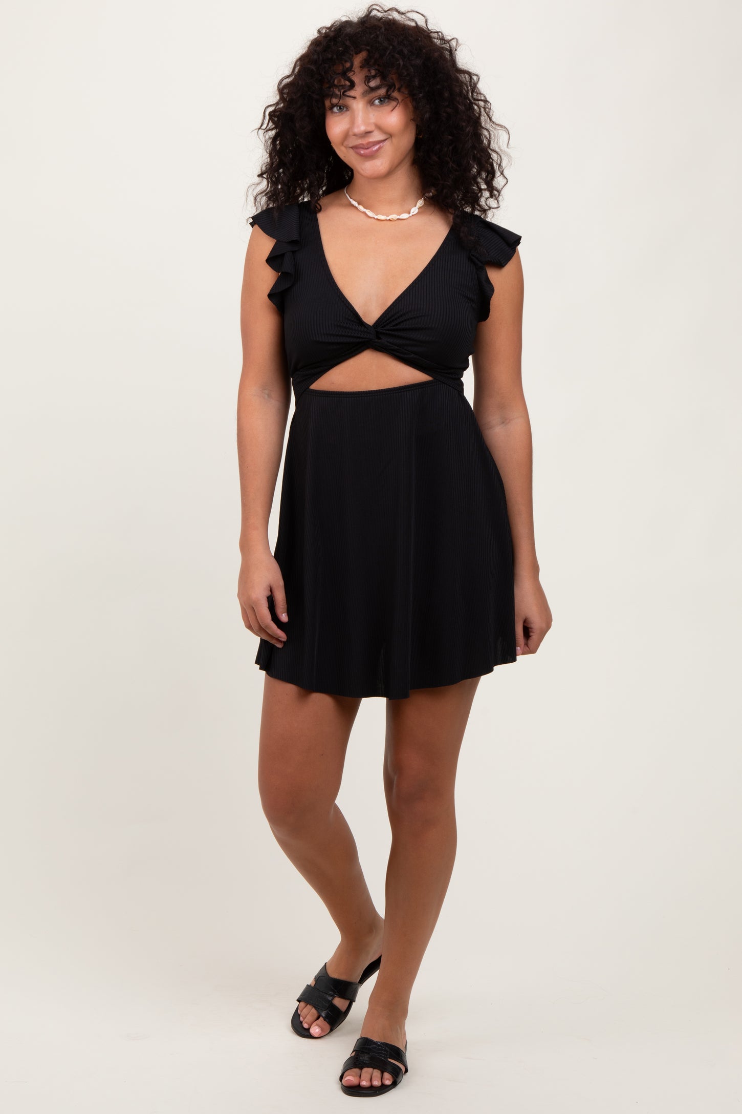 woman wearing a black short dress with ruffle sleeves and a cut-out design, paired with black sandals