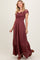 woman wearing a burgundy maxi dress with a smocked bodice, flutter sleeves, and button details, standing and smiling