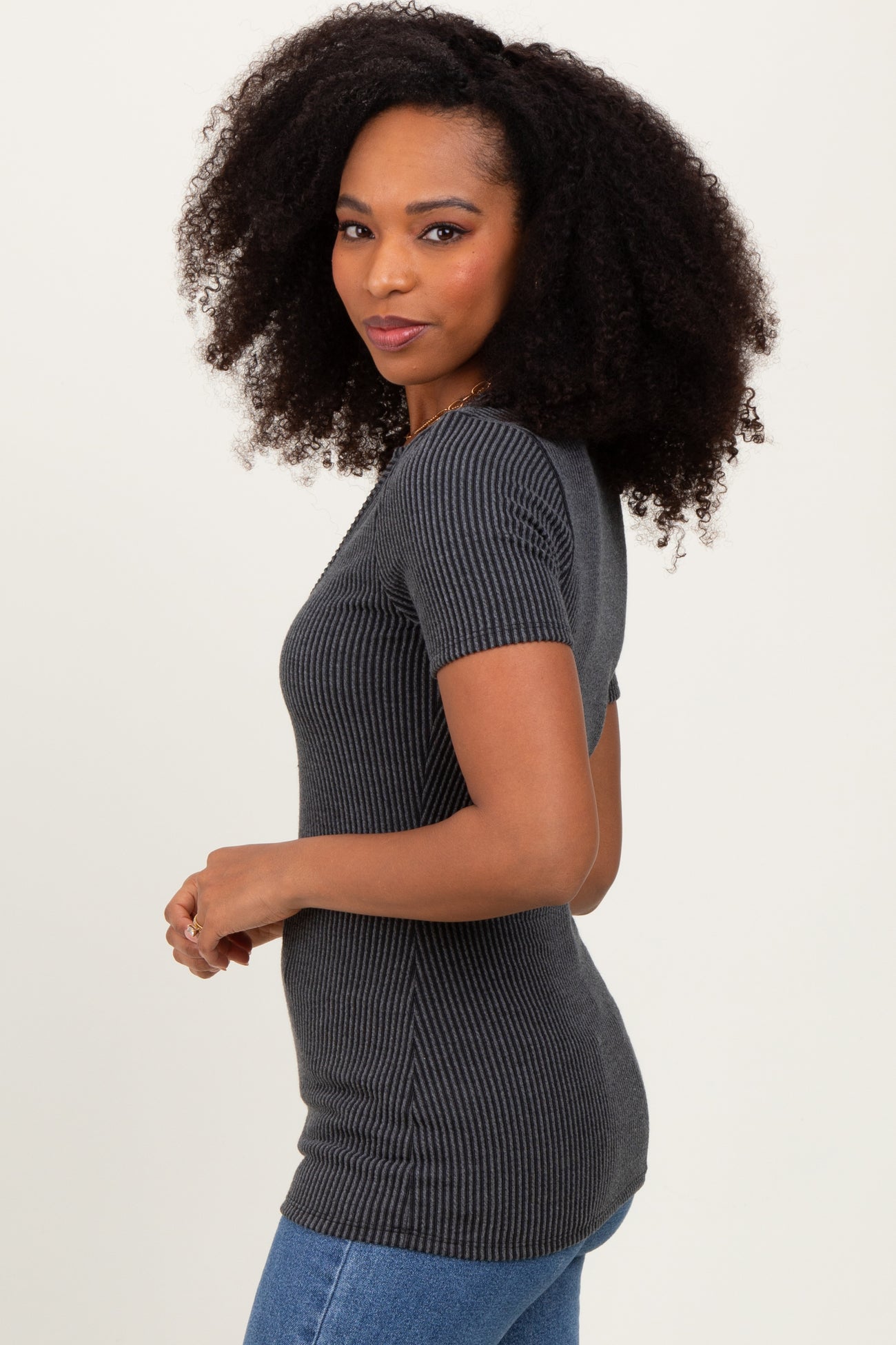 woman wearing a charcoal gray ribbed short sleeve top with fitted style and standing sideways against a plain background