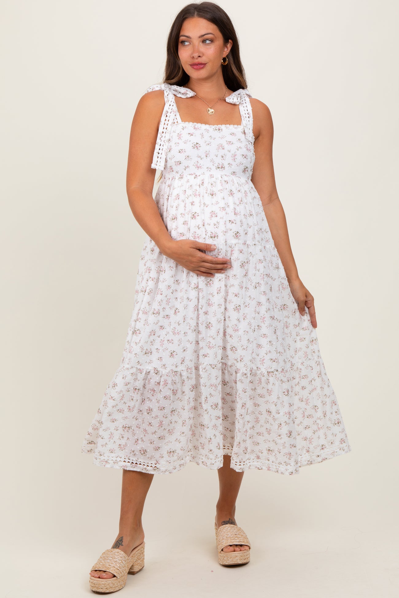 woman wearing a white floral maternity dress with tie straps and a visible baby bump