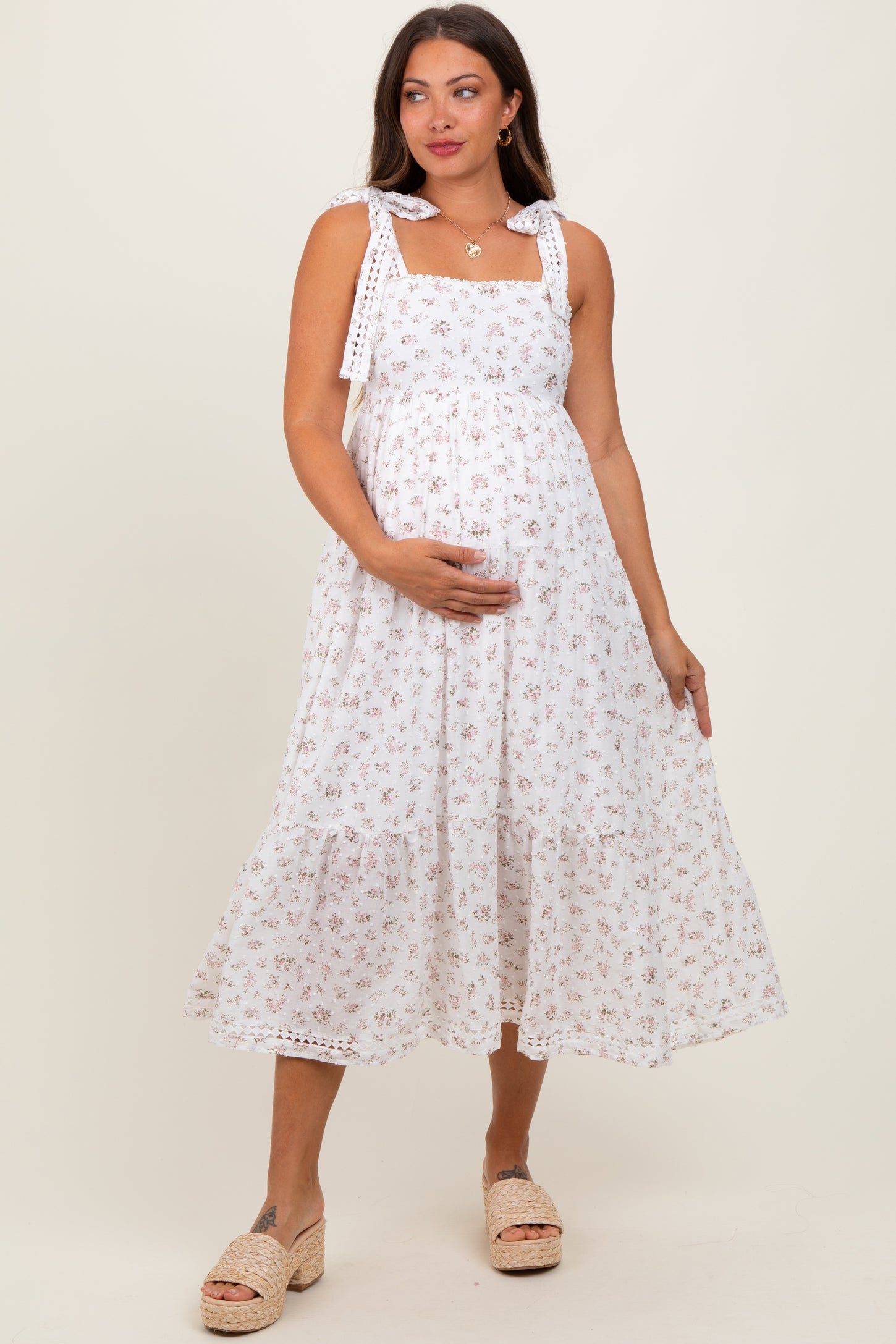 woman wearing a white floral maternity dress with tie straps and a visible baby bump