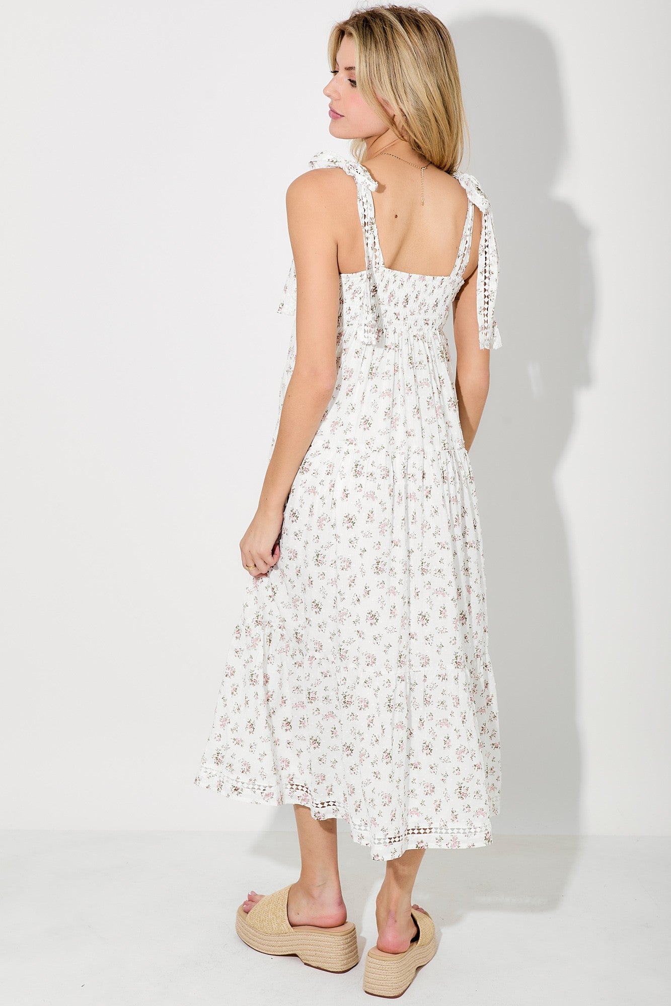 woman wearing a white floral midi dress with tie straps and a ruffled hem, standing with her back to the camera