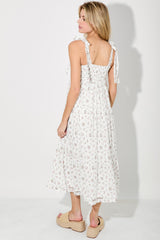 woman wearing a white floral midi dress with tie straps and a ruffled hem, standing with her back to the camera