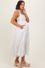 woman wearing a white floral maternity dress with tie straps and pockets, showcasing her baby bump