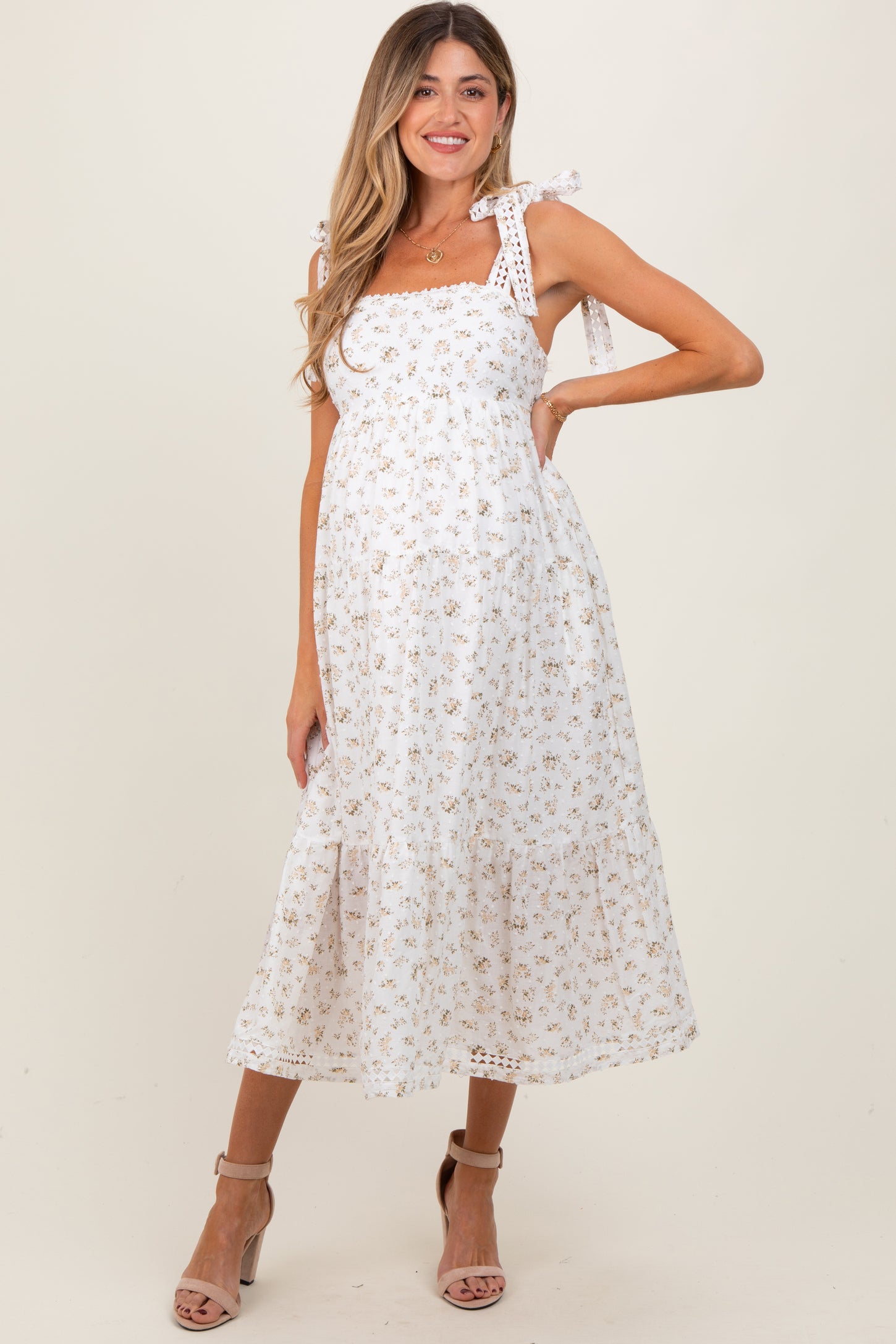 woman wearing a white floral print maternity dress with tie straps and a flowing skirt, highlighting her baby bump