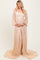 woman wearing a sheer beige lace maternity gown with long sleeves and a flowing train, holding her baby bump