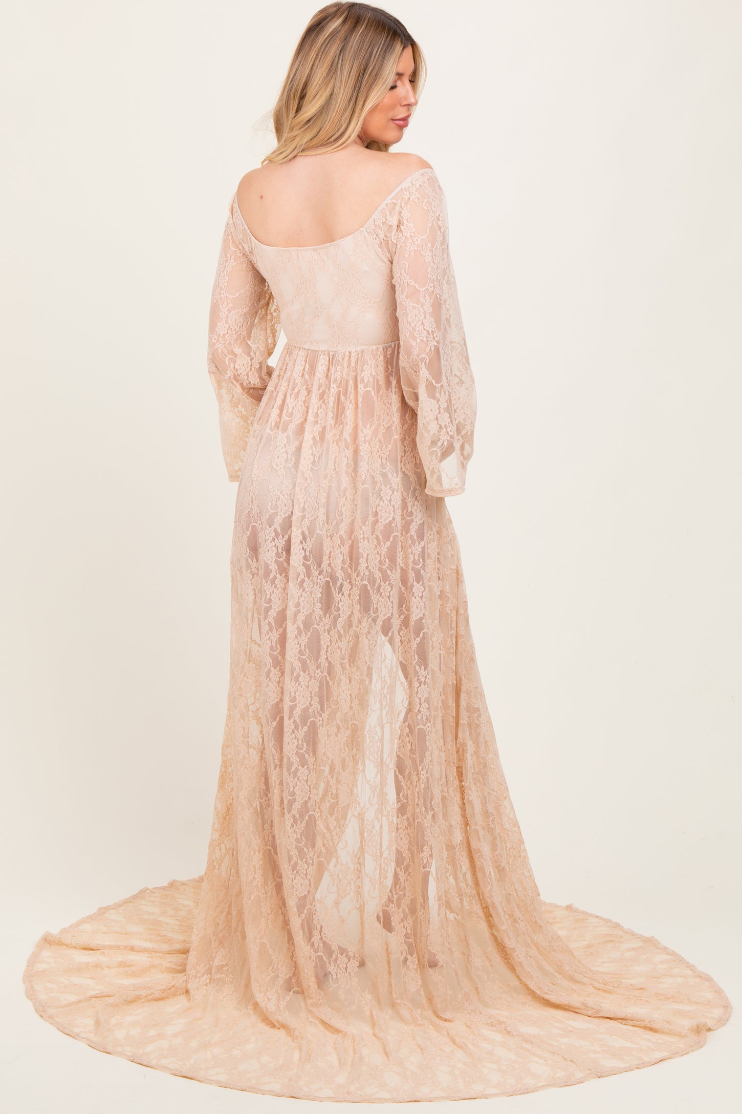 woman wearing a sheer nude lace maternity gown with long sleeves and a flowing train, showcasing a baby bump