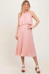 woman wearing a light pink pleated midi dress with a halter neck and layered top, standing in a neutral background