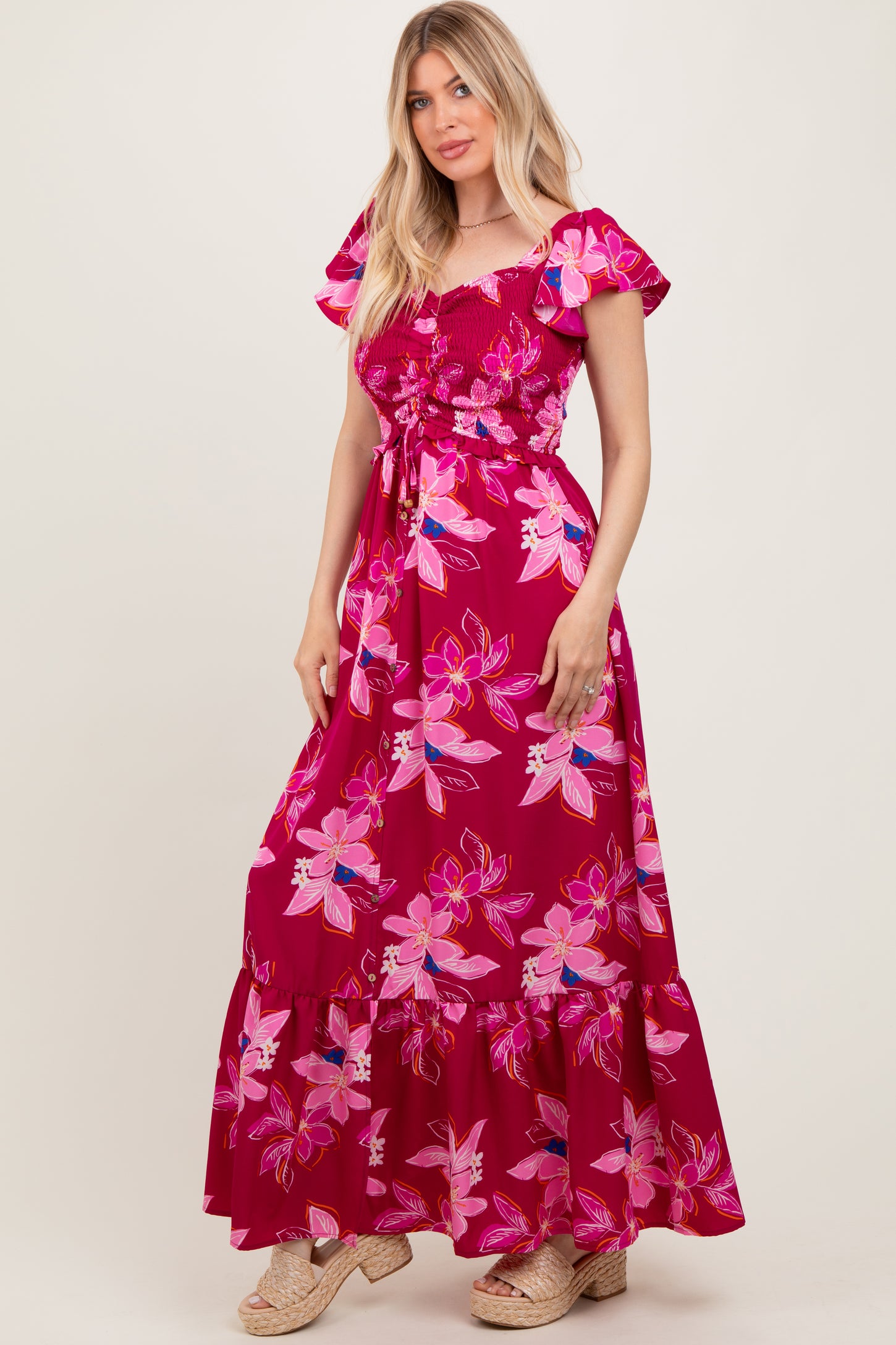 woman wearing a fuchsia floral maxi dress with short puff sleeves and a tie waist
