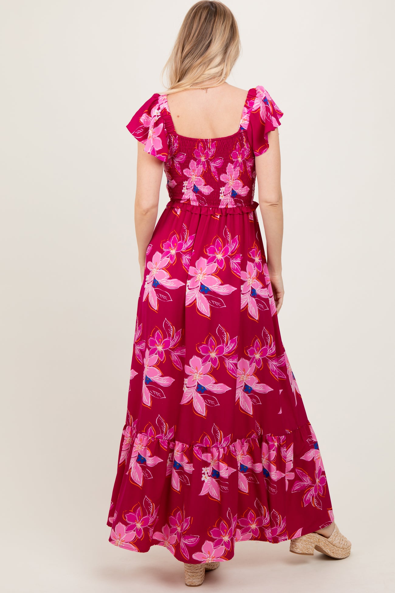 woman wearing a pink floral maxi dress with ruffled sleeves and a tie waist, shown from the back
