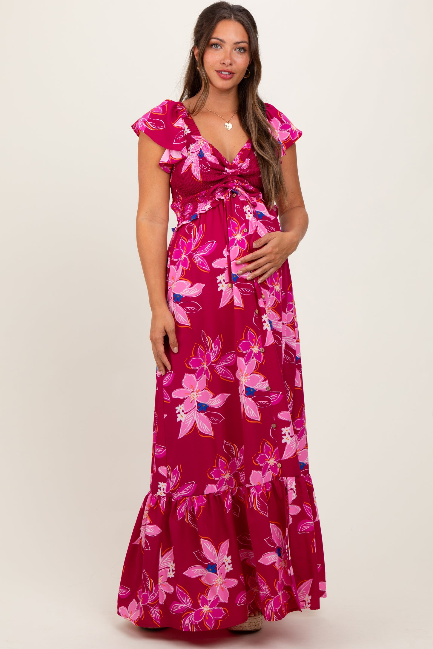 woman wearing a floral pink maternity maxi dress with flutter sleeves and a tie front, showing her baby bump