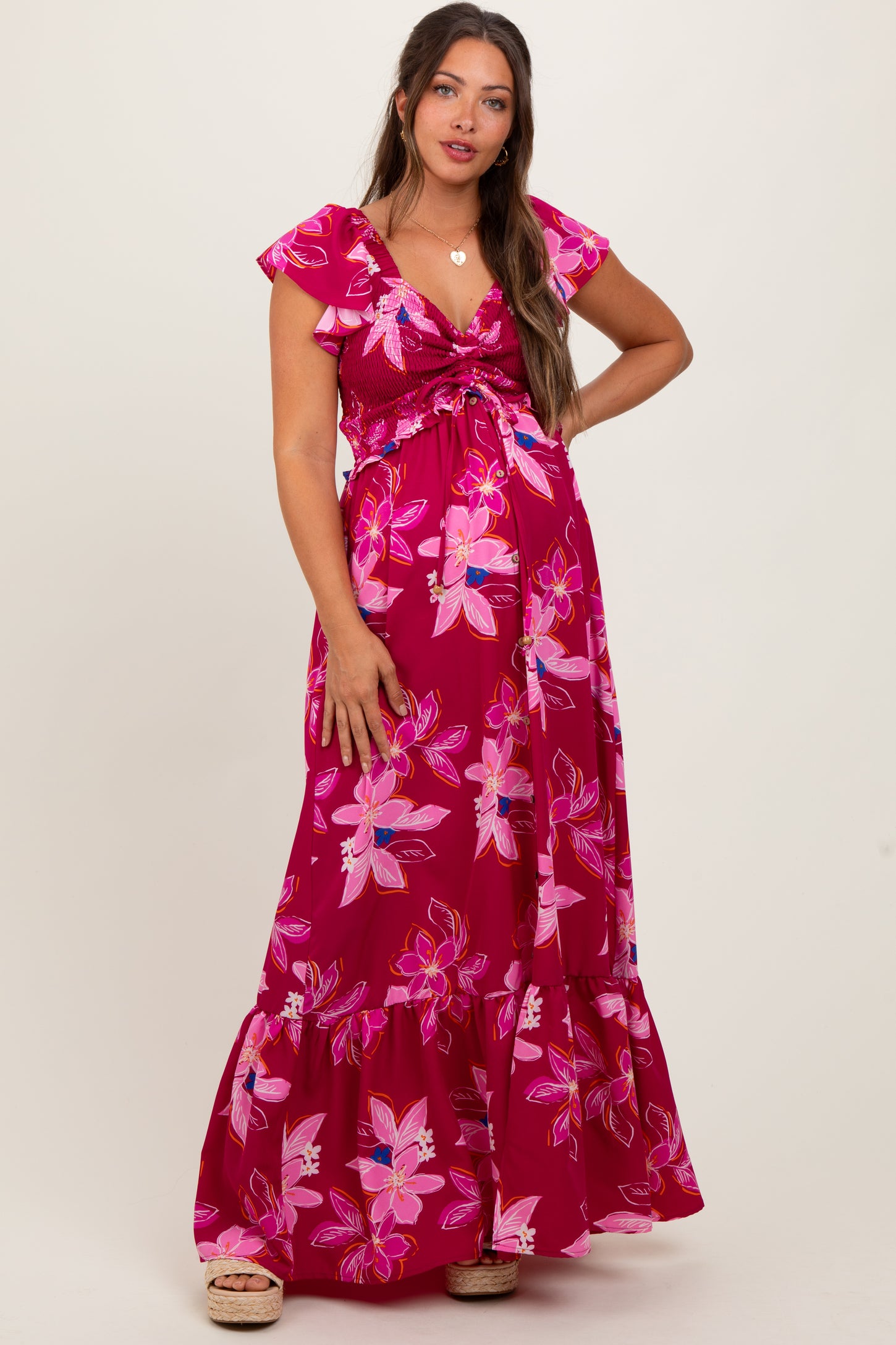 woman wearing a pink floral maternity maxi dress with flutter sleeves and a tie front, showing her baby bump