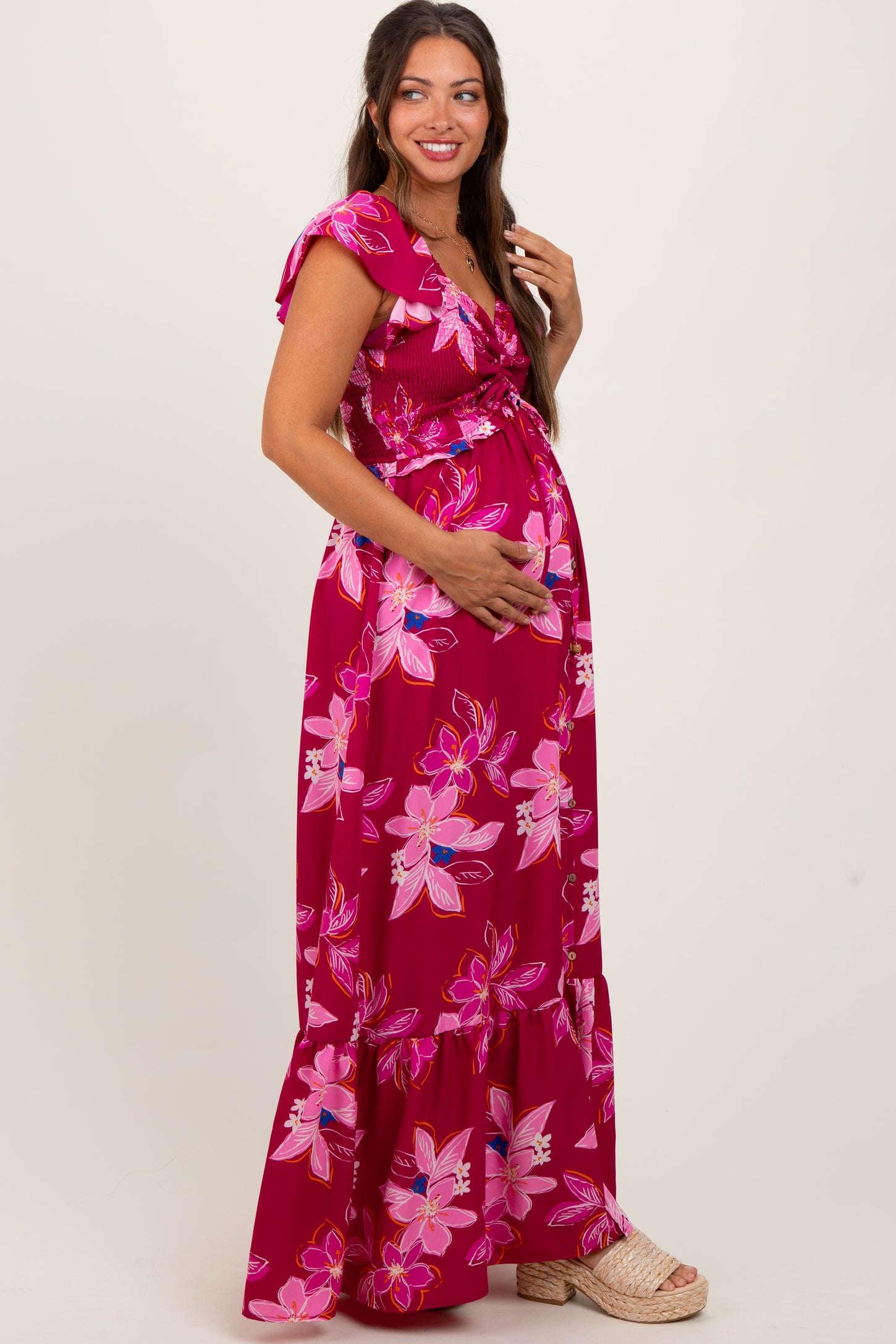 woman wearing a fuchsia floral print maternity maxi dress and holding her baby bump