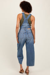 woman wearing a green tank top and blue denim overalls, showing the back view and relaxed fit of the outfit