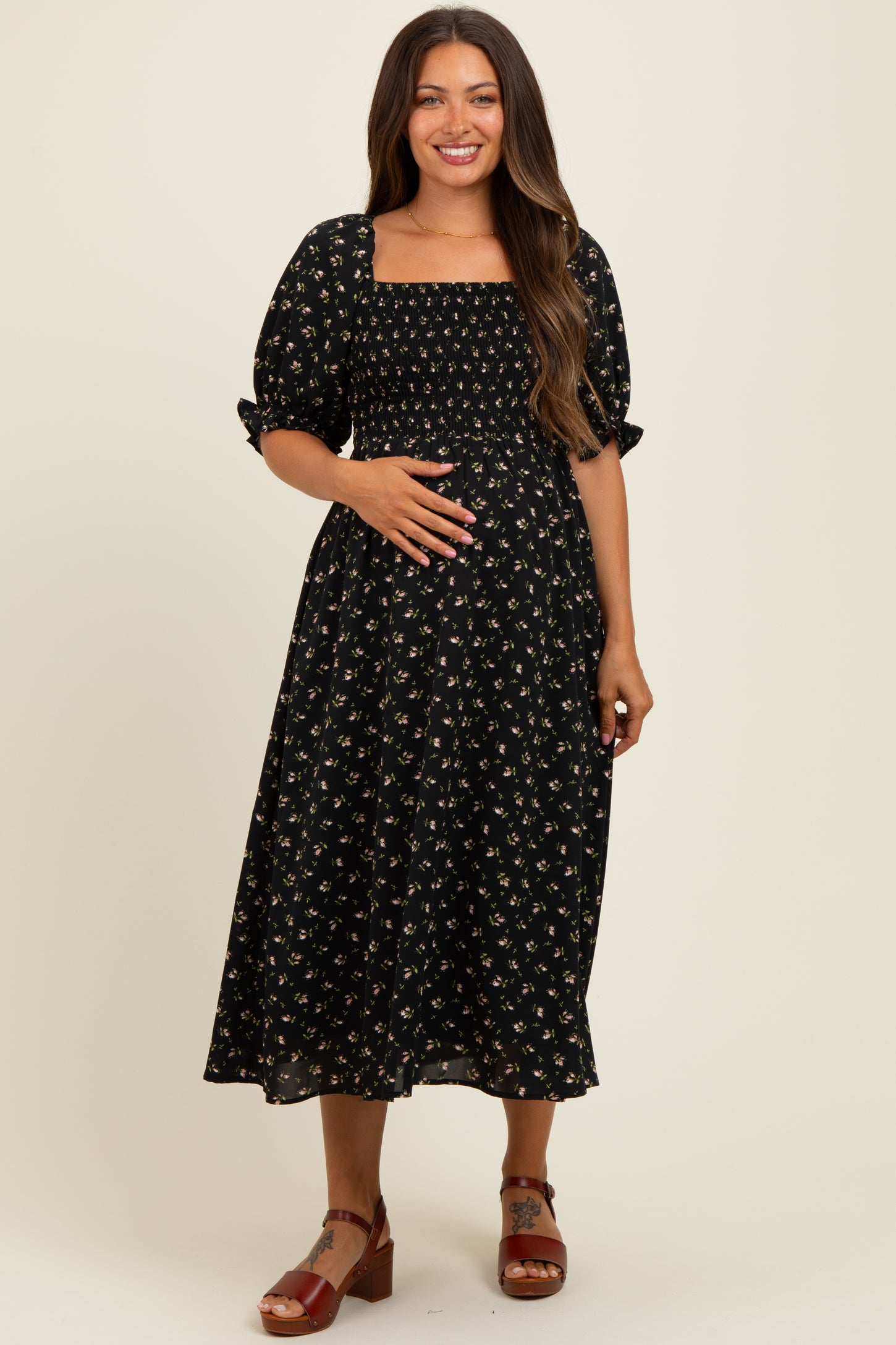 woman wearing a black floral maternity dress with smocked bodice and puff sleeves, showcasing her baby bump