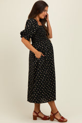 woman wearing a black floral smocked maternity dress with puff sleeves and pockets, showing her baby bump