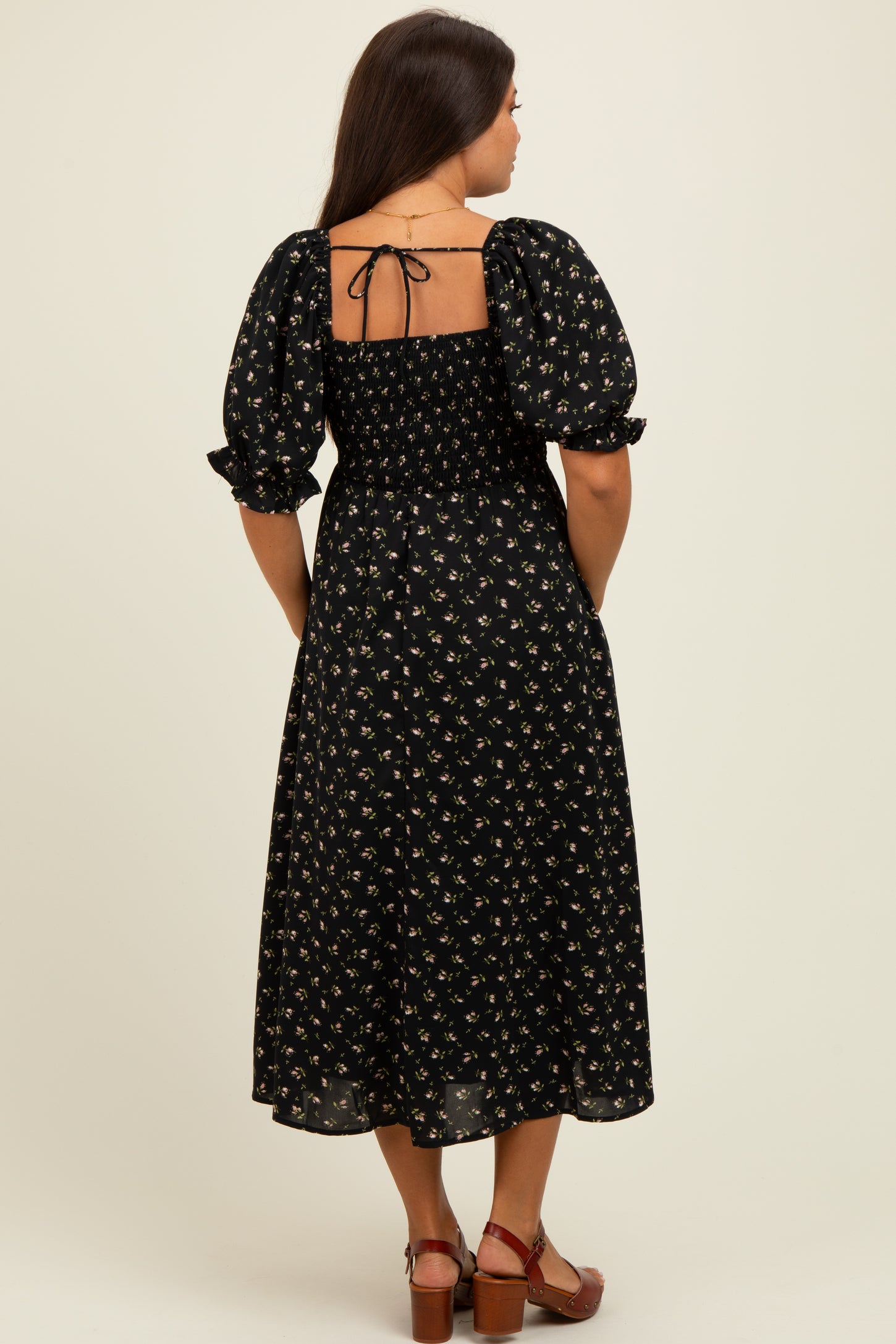 woman wearing a black floral maternity dress with puff sleeves and a smocked back, showing a baby bump