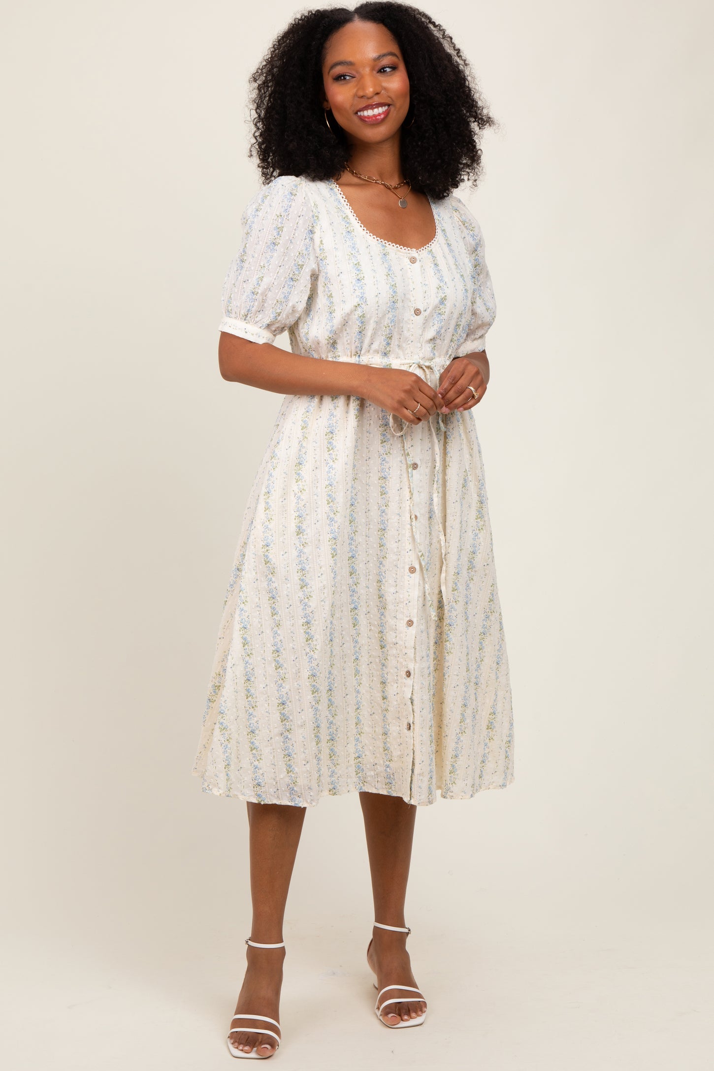 woman wearing a white floral patterned midi dress with puff sleeves and buttons down the front, smiling at the camera