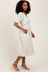 woman wearing a cream-colored midi dress with floral print and a tie waist, styled with sandals and curly hair