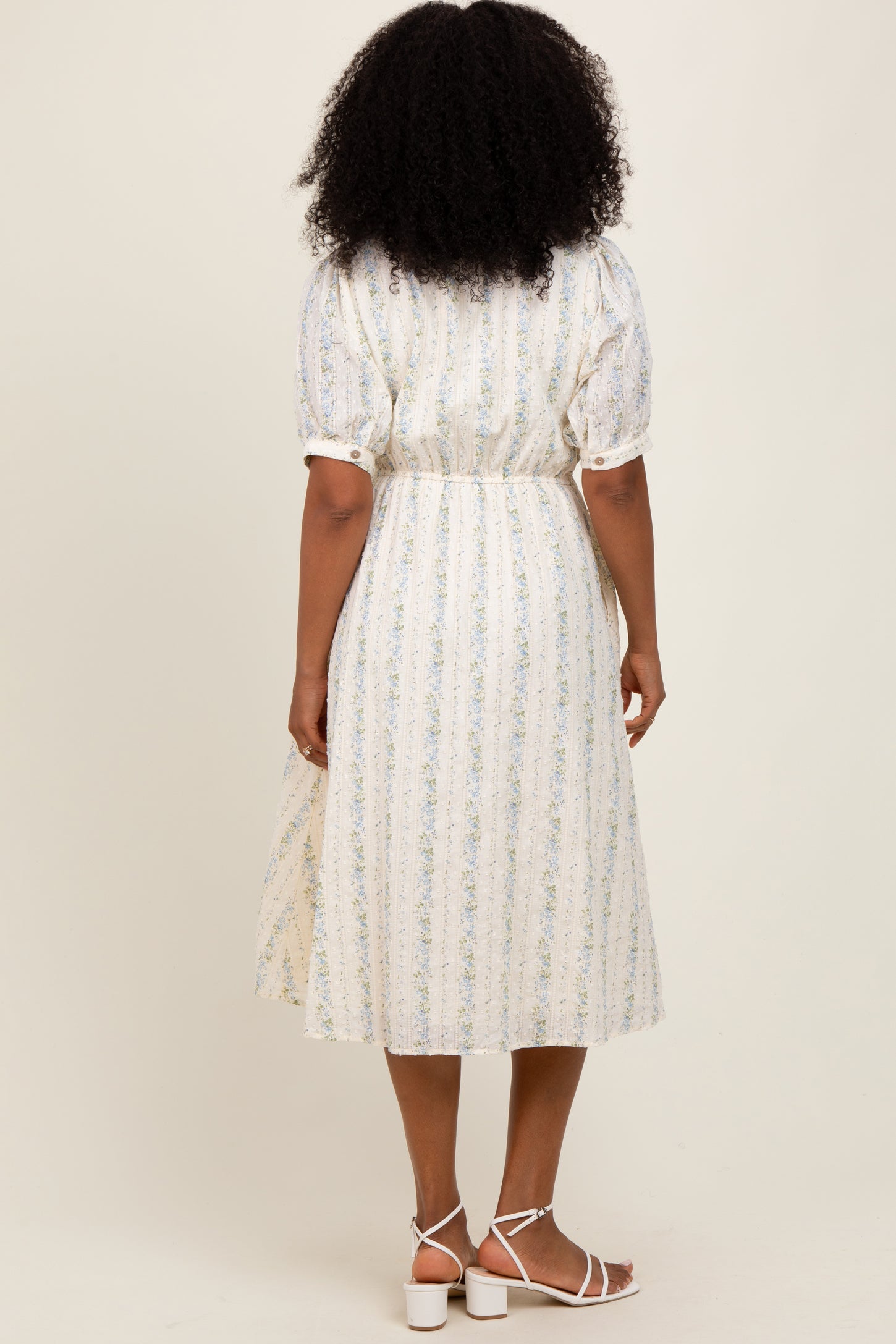 woman wearing a white midi dress with blue floral stripes and puff sleeves, standing with her back facing the camera