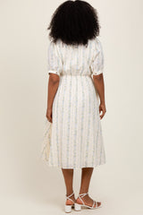 woman wearing a white midi dress with blue floral stripes and puff sleeves, standing with her back facing the camera