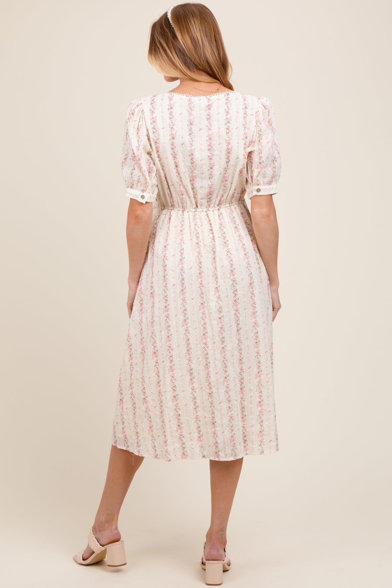 woman wearing a cream floral print maternity dress with puff sleeves and a cinched waist, showing a baby bump