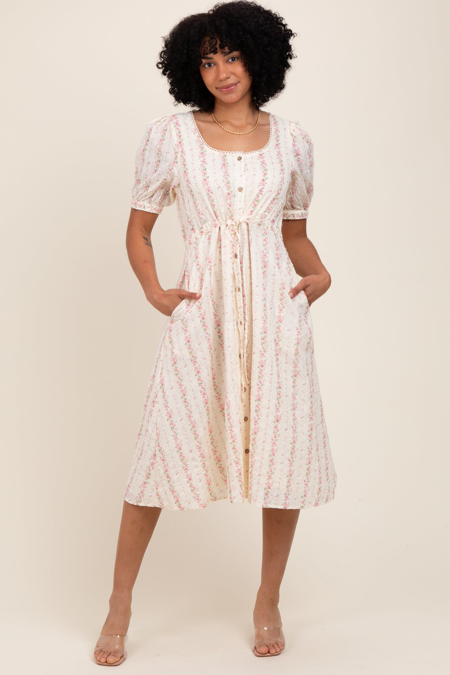 woman wearing a cream floral print midi dress with puff sleeves and a button-down front, featuring pockets