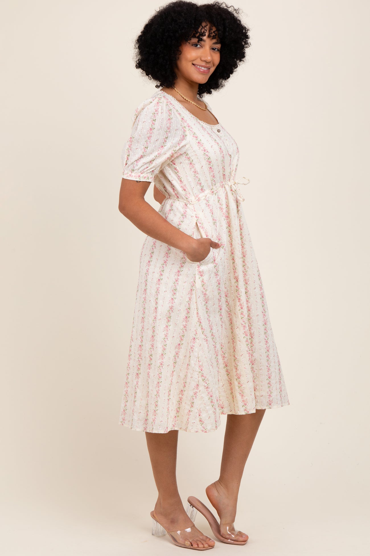 woman wearing a cream floral midi dress with short puff sleeves and a drawstring waist, standing in profile