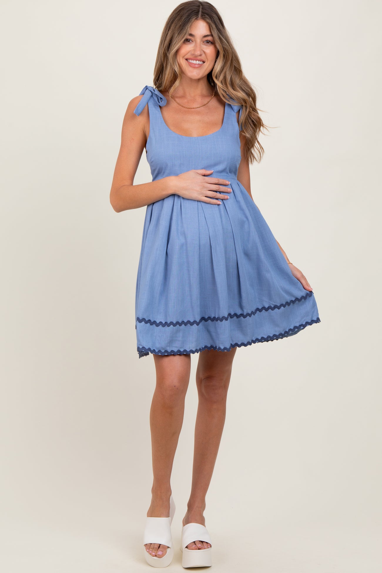 woman wearing a light blue maternity dress with tie shoulder straps and a pleated skirt, showing her baby bump