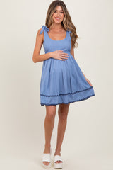 woman wearing a light blue maternity dress with tie shoulder straps and a pleated skirt, showing her baby bump