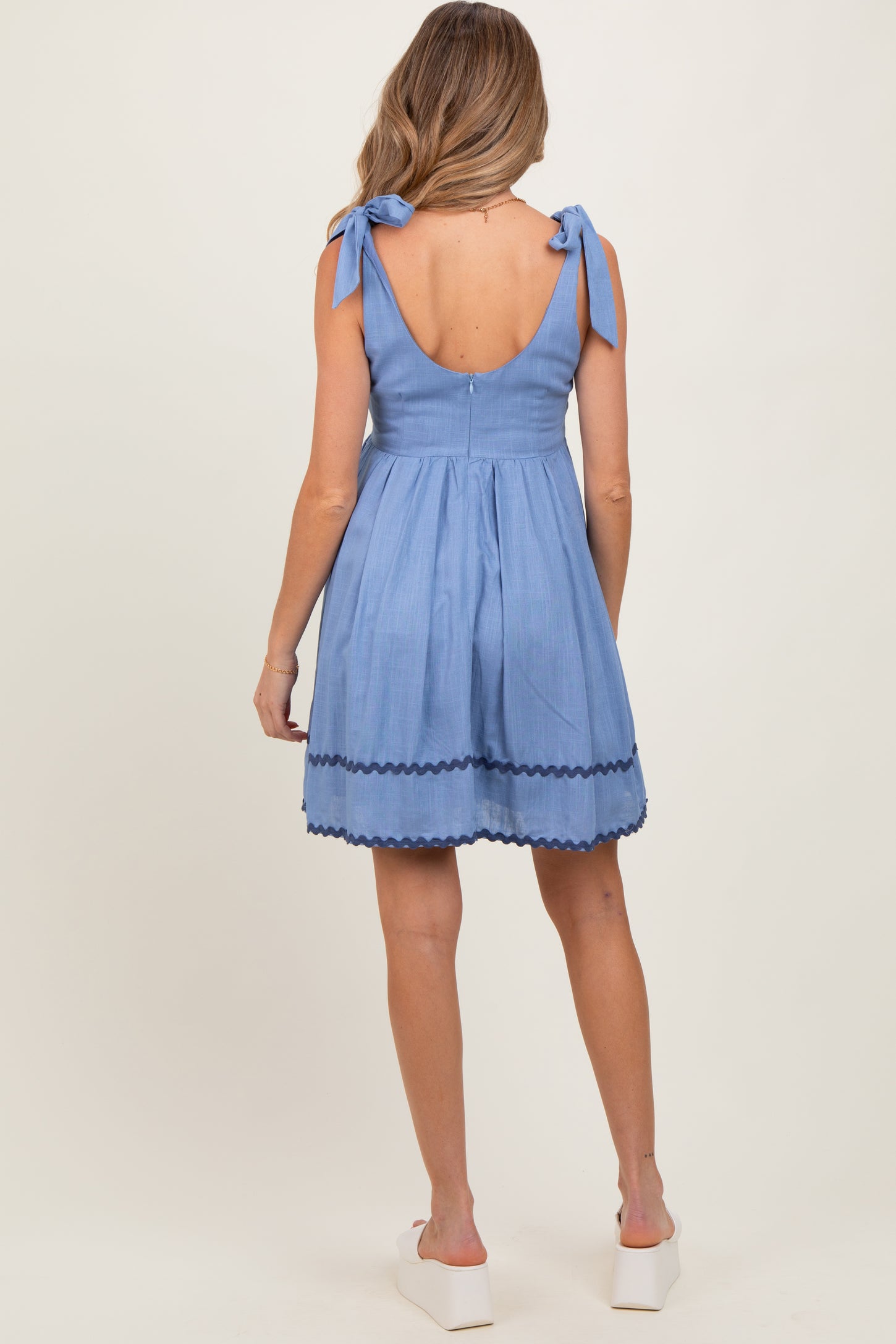 woman wearing a blue maternity dress with tie straps and scalloped hem, shown from the back