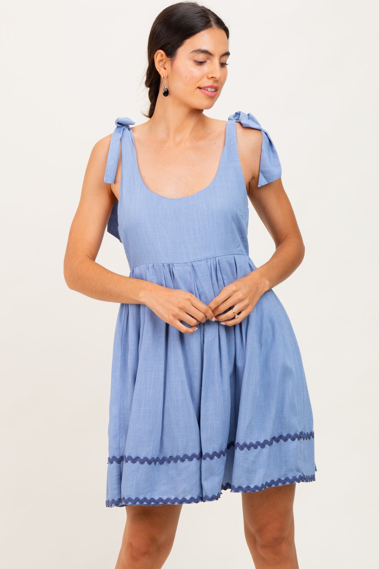 woman wearing a light blue sleeveless dress with tie straps and ric rac trim at the hem