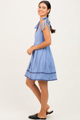 woman wearing a light blue sleeveless dress with ties on the shoulders and scalloped hem, smiling and standing sideways