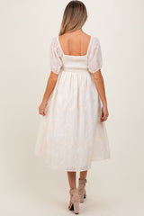 woman wearing a white maternity dress with puff sleeves and floral embroidery, showcasing the back view