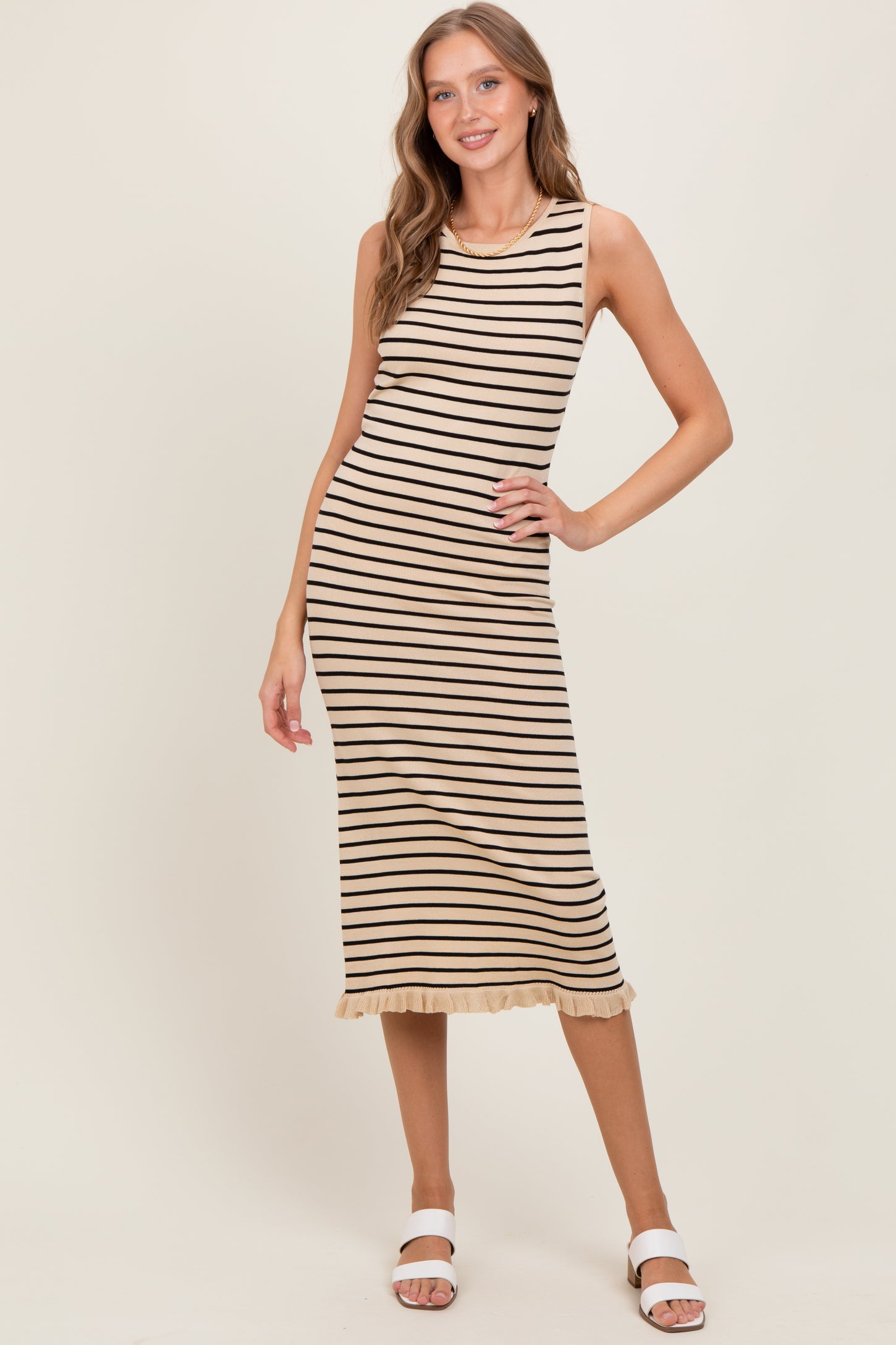 woman wearing a beige and black striped sleeveless midi dress with a ruffled hem and white sandals