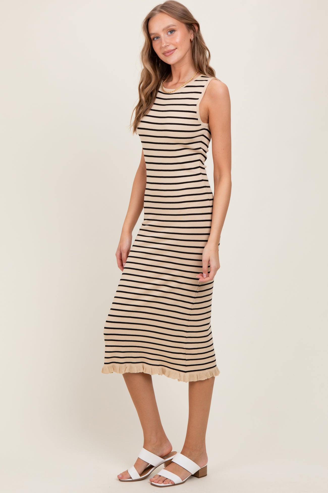 woman wearing a beige and black striped sleeveless midi dress with a ruffled hem and white sandals