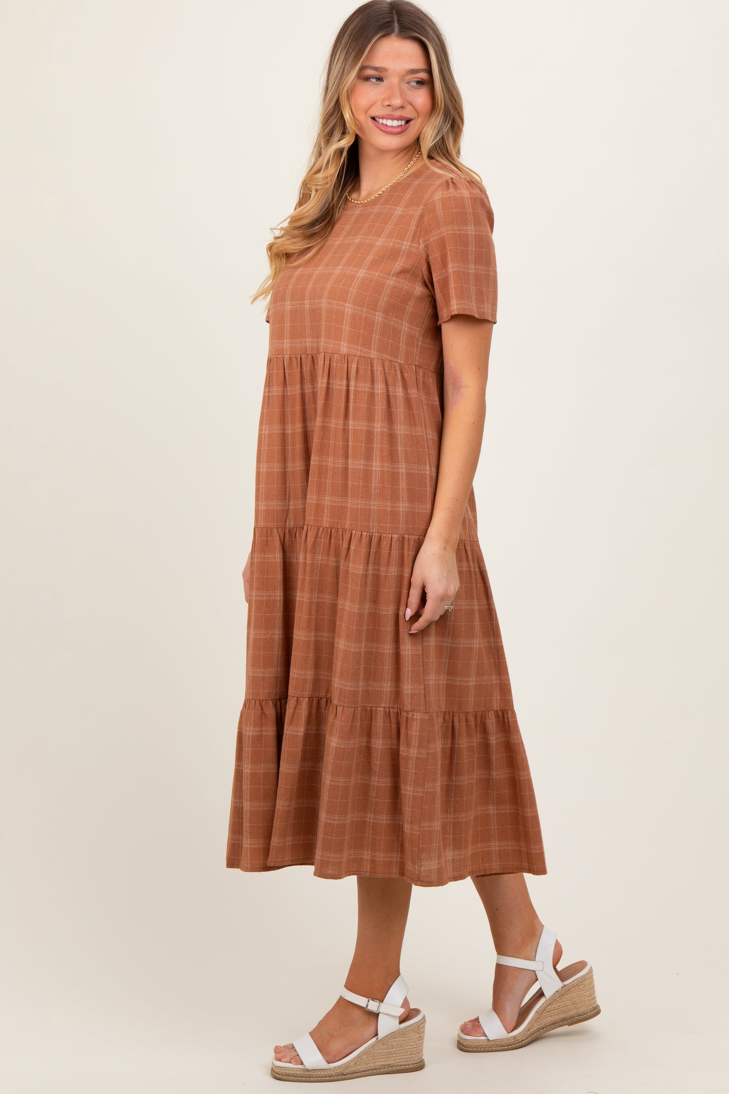 woman wearing a rust-colored short sleeve tiered midi dress with a checkered pattern and white espadrille wedges