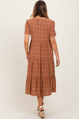 woman wearing a brown plaid tiered midi dress with short sleeves and a button detail at the back