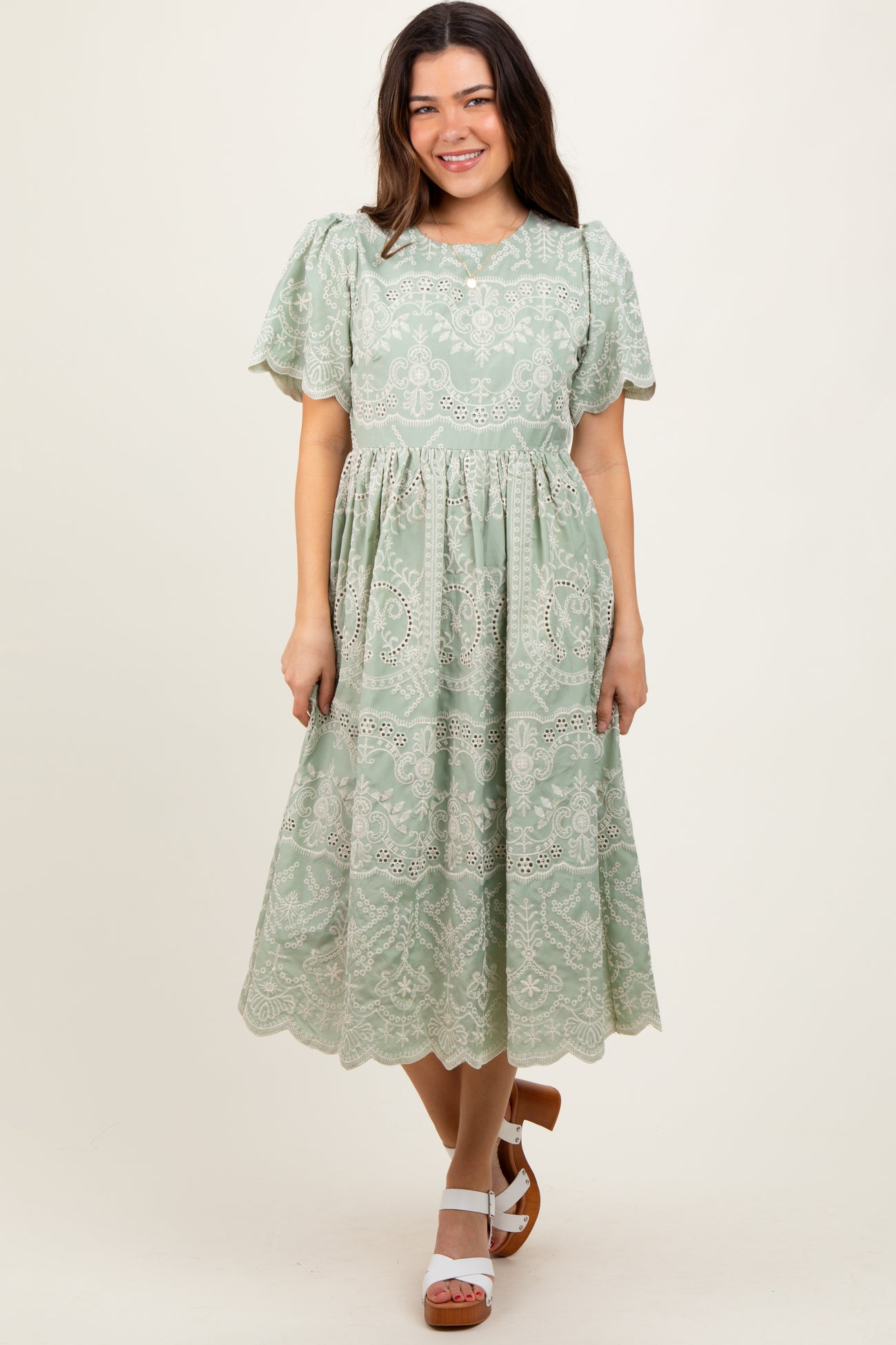 woman wearing a green lace midi dress with puff sleeves and a tiered skirt, standing and smiling