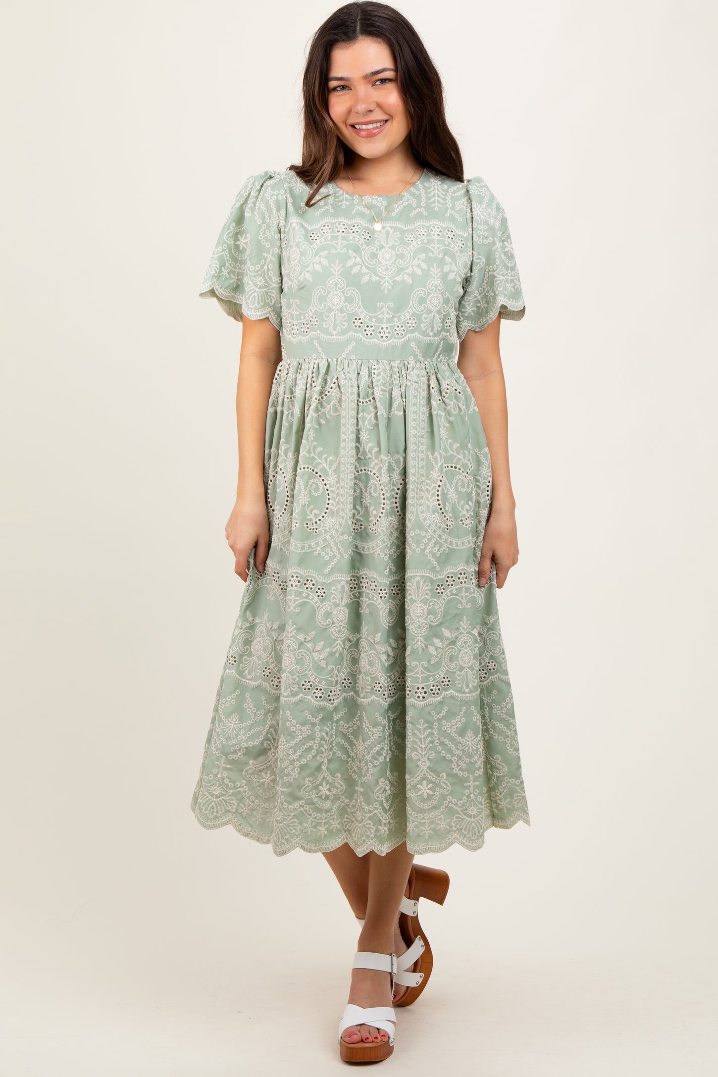 woman wearing a green lace midi dress with puff sleeves and a tiered skirt, standing and smiling