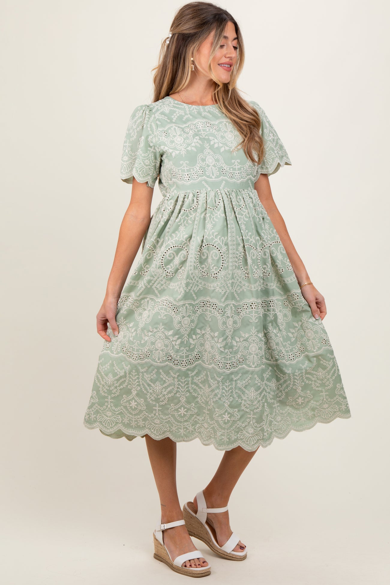 woman wearing a light green maternity dress with short sleeves and lace detailing, standing in a relaxed pose