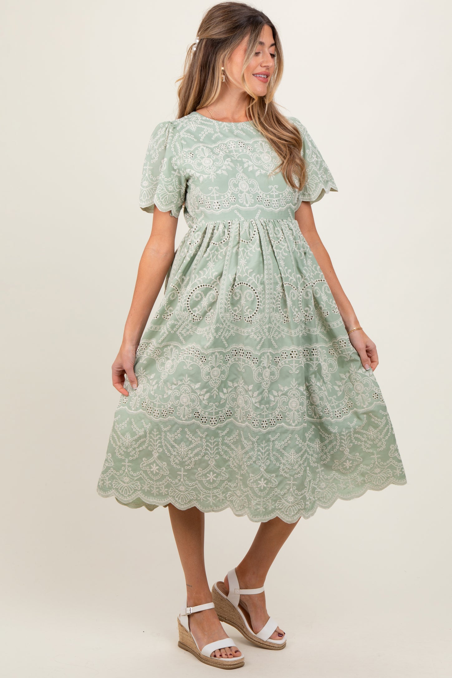 woman wearing a light green maternity dress with short sleeves and lace detailing, standing in a relaxed pose