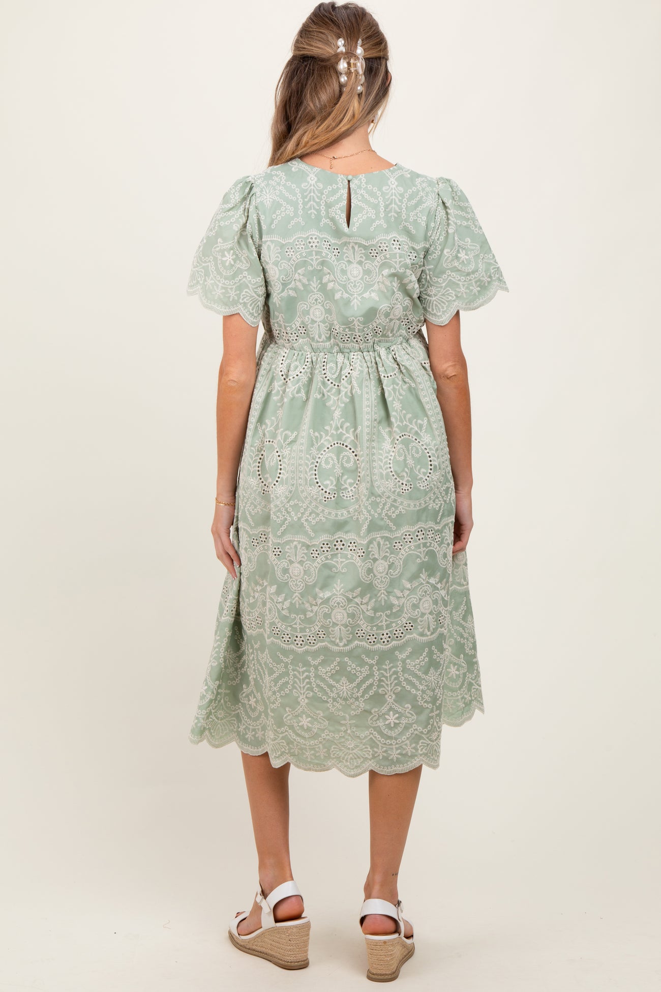 woman wearing a sage green maternity dress with lace details and short sleeves, view of the back