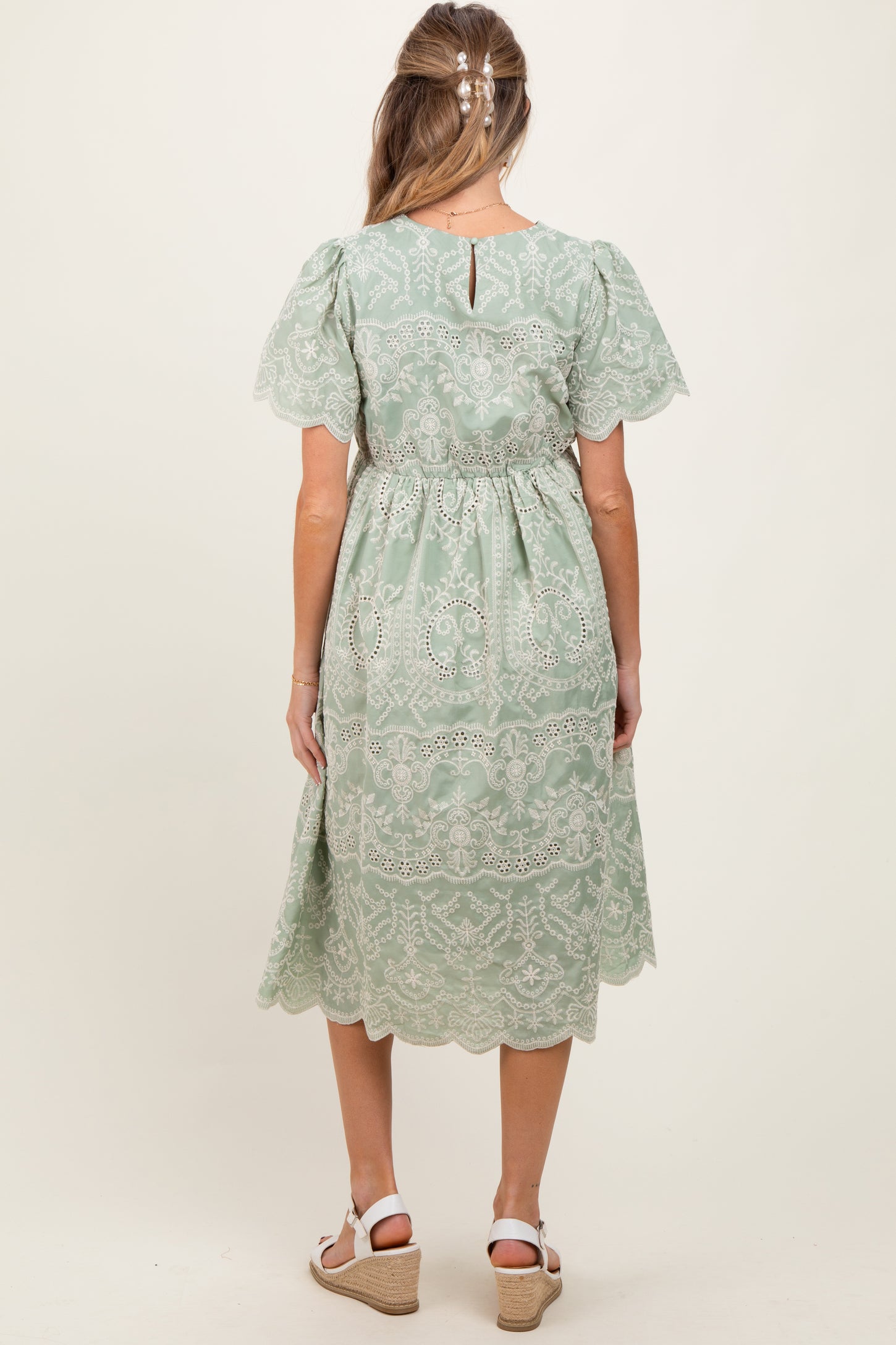 woman wearing a sage green maternity dress with lace details and short sleeves, view of the back