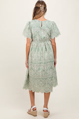 woman wearing a sage green maternity dress with lace details and short sleeves, view of the back