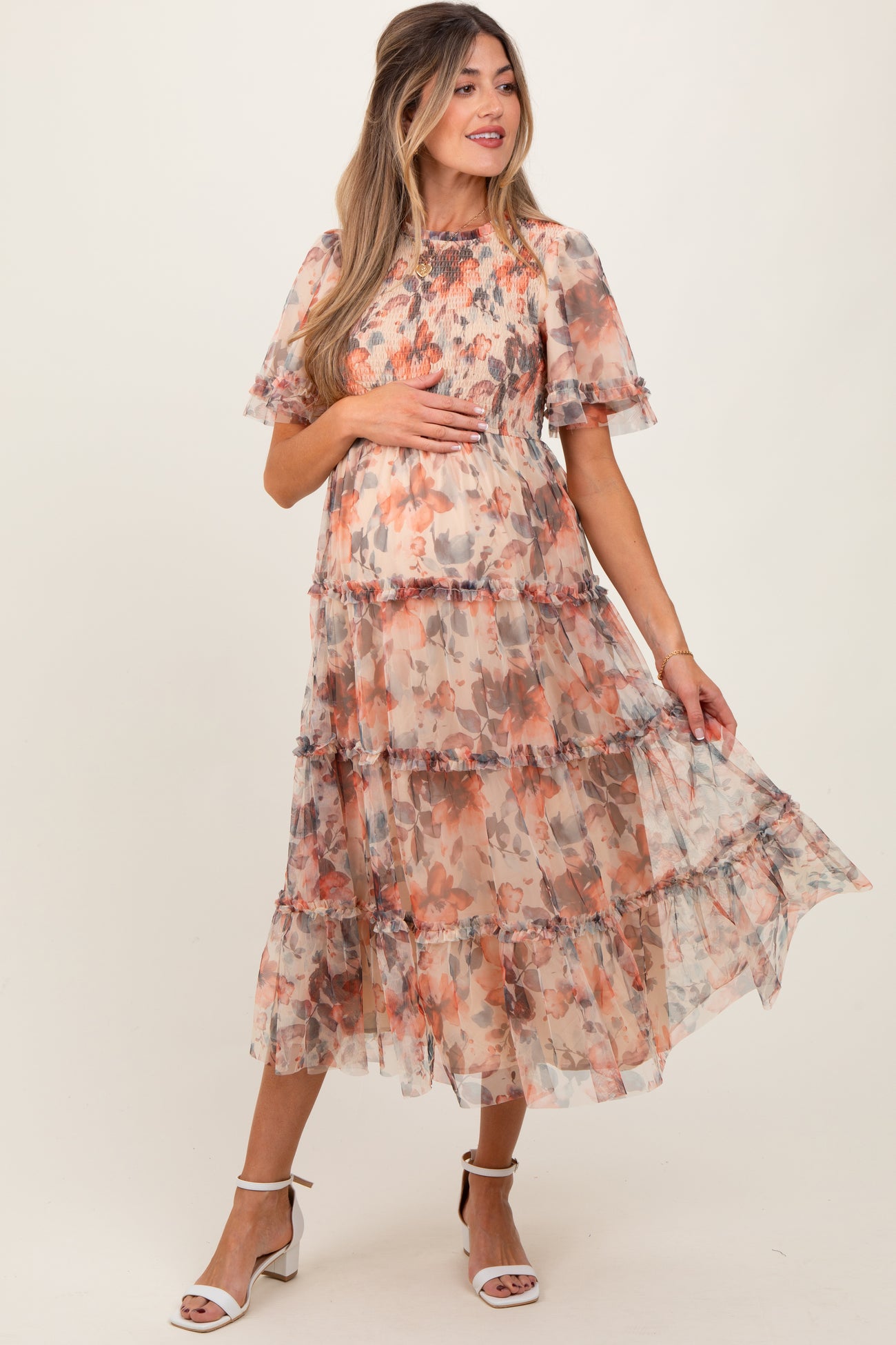 woman wearing a floral tiered maternity dress with short sleeves and holding her baby bump